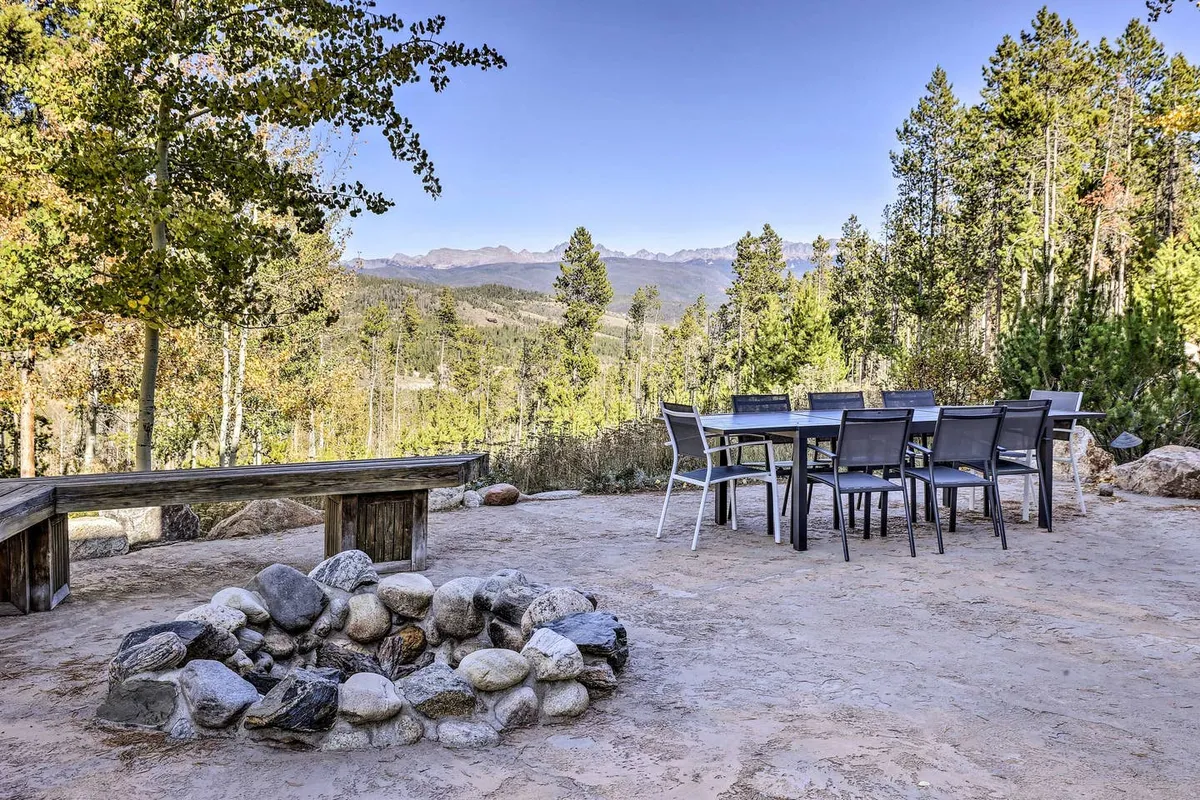 A tranquil outdoor living area featuring a fire pit, outdoor dining table, and breathtaking mountain views. Surrounded by mature trees, the space invites families and groups to gather for sunset dinners, fireside chats, or early morning coffee while enjoying the sights and sounds of nature.