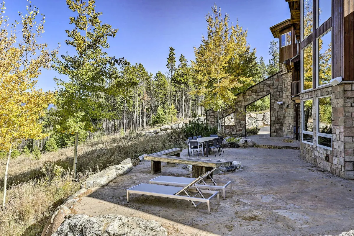 An expansive stone terrace with outdoor seating, surrounded by aspen trees and featuring a dramatic mountain view. The setting is ideal for al fresco dining, relaxation, and appreciating panoramic vistas, reinforcing the luxurious and curated experience offered to guests.