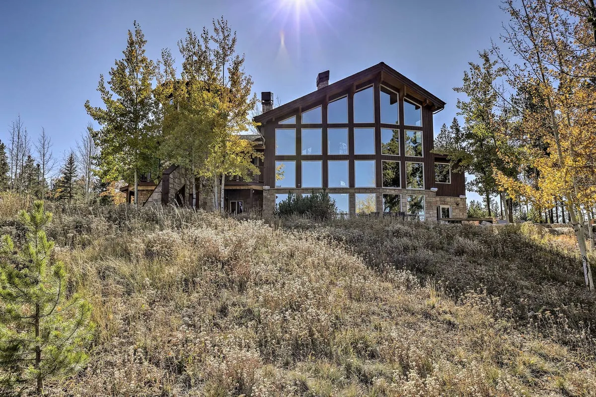 This exterior image showcases a modern home surrounded by aspen trees and natural landscaping, with large glass windows that suggest expansive indoor-outdoor views. The serene mountain setting is evident, with hints of sunset colors and a tranquil ambiance for outdoor gatherings or relaxation.