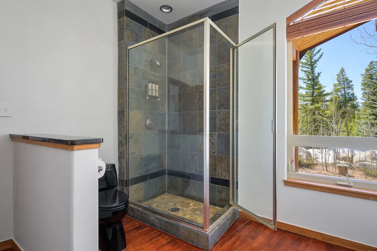 A luxurious bathroom with a glass shower enclosure, natural light streaming in from a window, and tasteful wooden accents that evoke a spa-like ambiance.