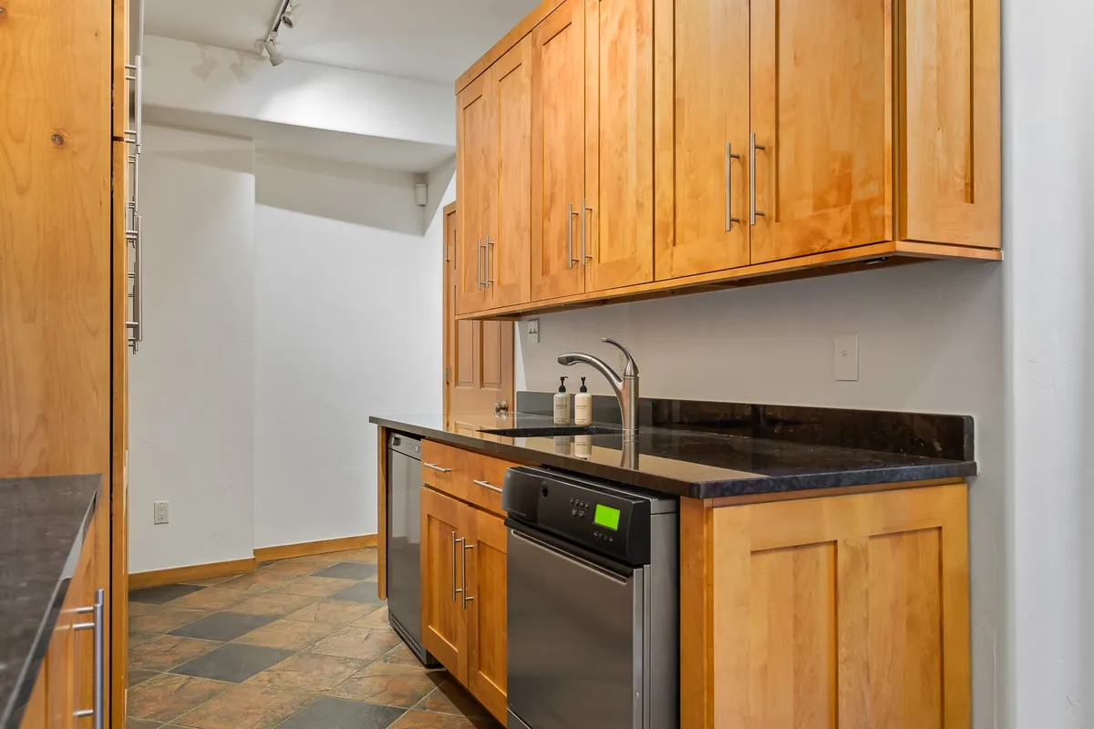 A spacious kitchen interior with sleek stainless steel appliances, black granite countertops, and custom wooden cabinetry. The space is arranged for both practical cooking and social entertaining, with room for group activities and celebrations.