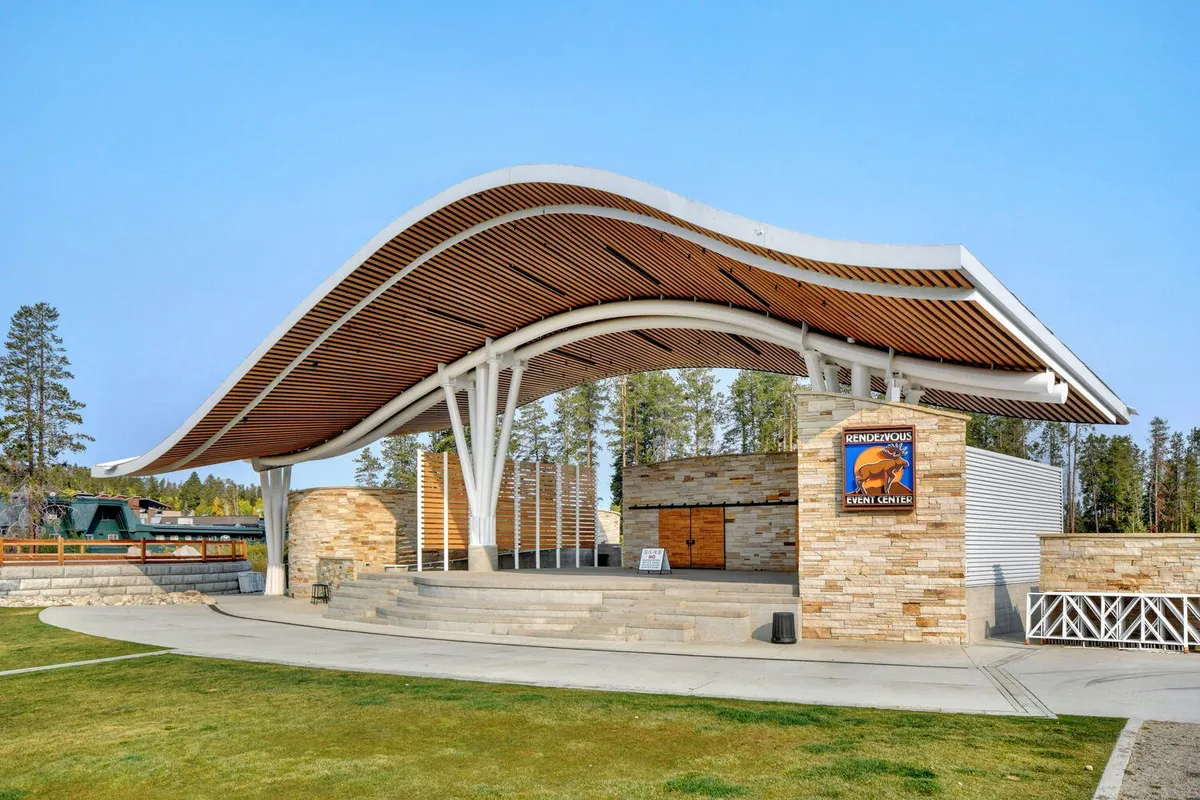 An exterior shot of a curved roof event center surrounded by stone walls, broad entrance steps, and clear event signage. The setting is vibrant and ready for community gatherings, performances, and seasonal festivals.