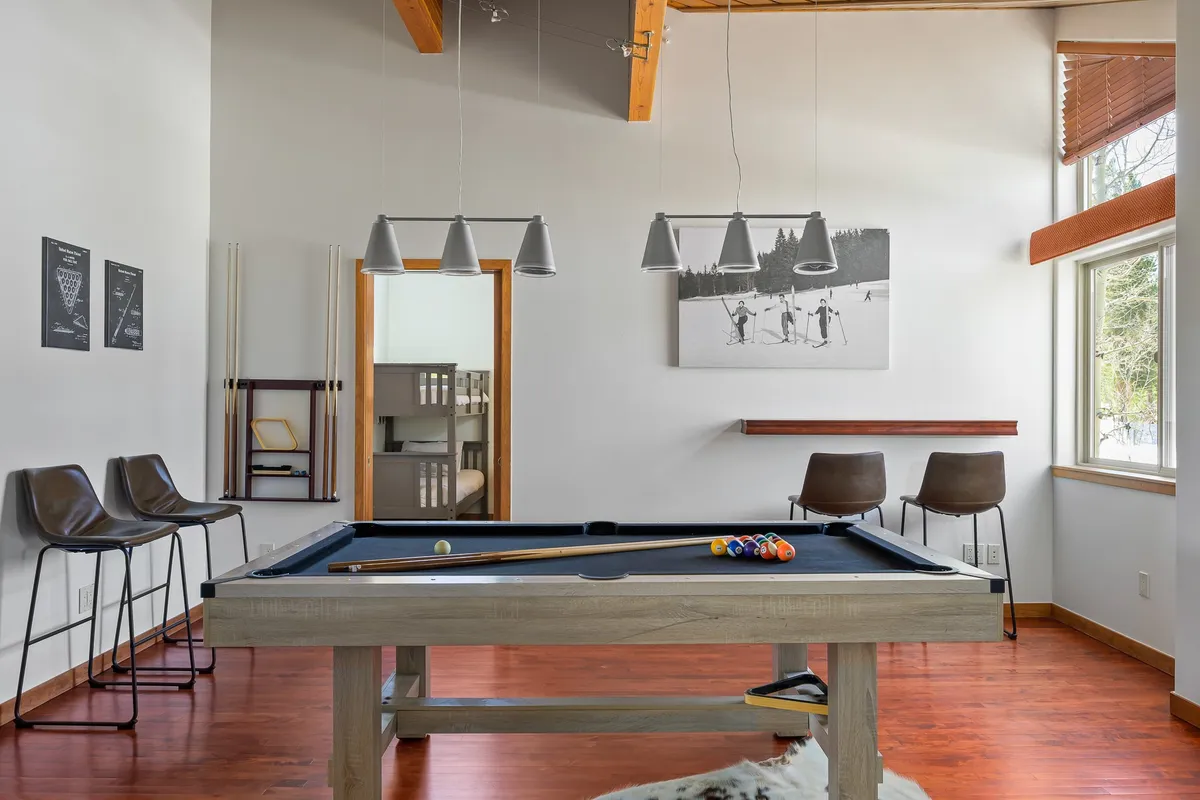 A vibrant, playful interior shot of a game room featuring a pool table, bar stools, and wall art. The space is designed for fun and social interaction, perfect for hosting friendly competitions and unwinding with friends or family after a day outdoors.