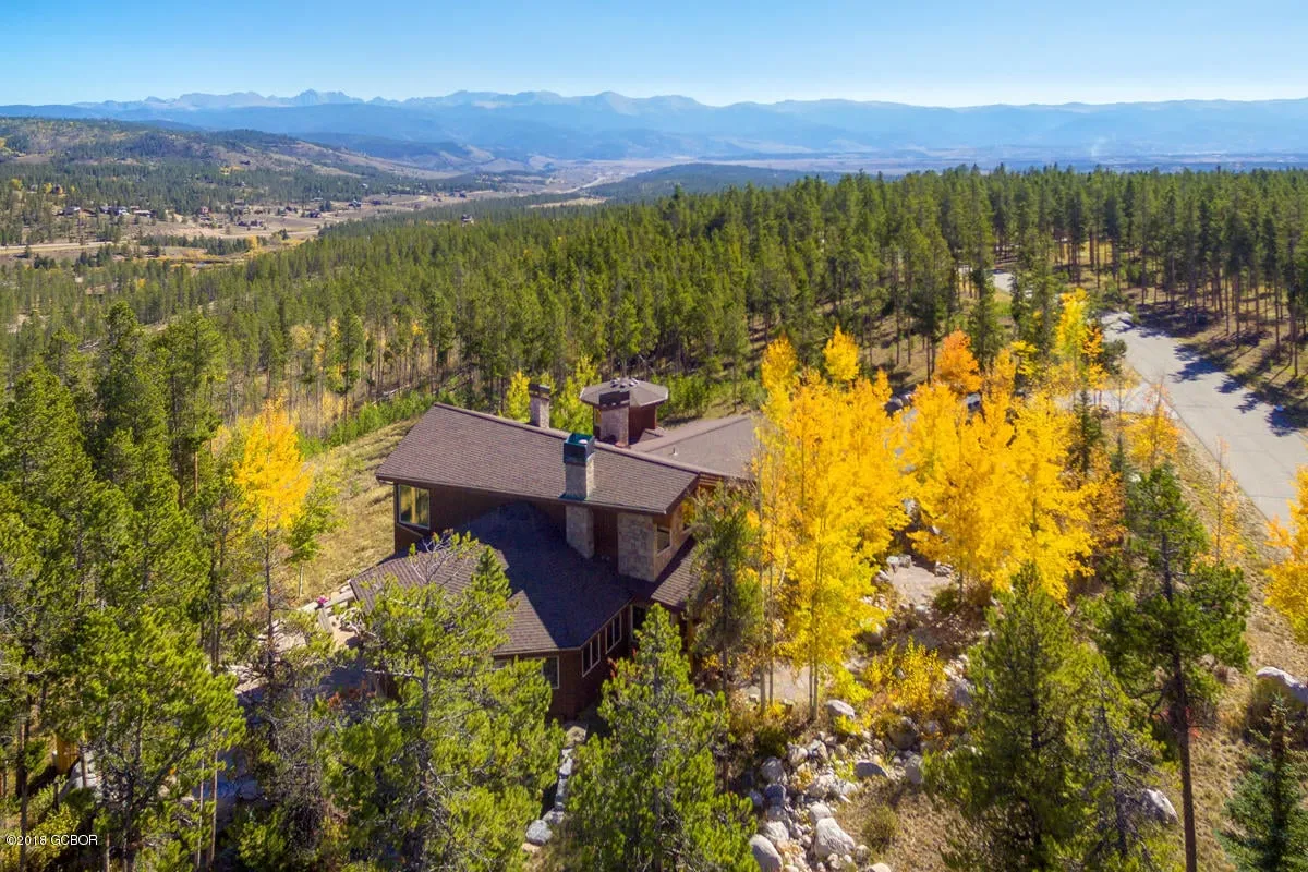 A serene exterior view of the home nestled among trees with distant mountains in the background and a welcoming porch. The landscape hints at seclusion and privacy while offering access to the natural beauty surrounding the property. The image evokes the sense of a private retreat with opportunities for relaxing outdoors and enjoying stunning sunset views.