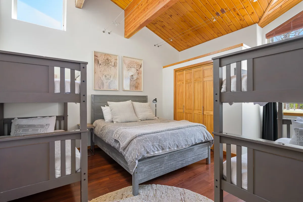 A cozy bunk room outfitted with stacked bunk beds, a main bed, wooden ceiling, and playful artwork. The arrangement is ideal for family sleepovers and provides a welcoming retreat for children and adults alike.