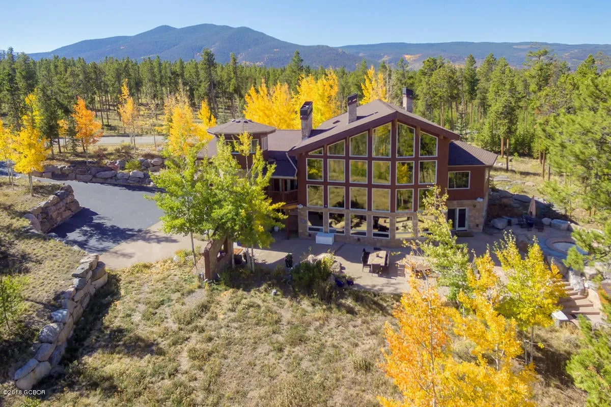 The hero image showcases the exterior of a luxurious single-family home nestled among tall trees, with expansive glass windows framing sweeping mountain vistas. A spacious patio invites guests to gather for sunset views, cozy evenings by the fire pit, or morning coffee surrounded by nature's majesty.