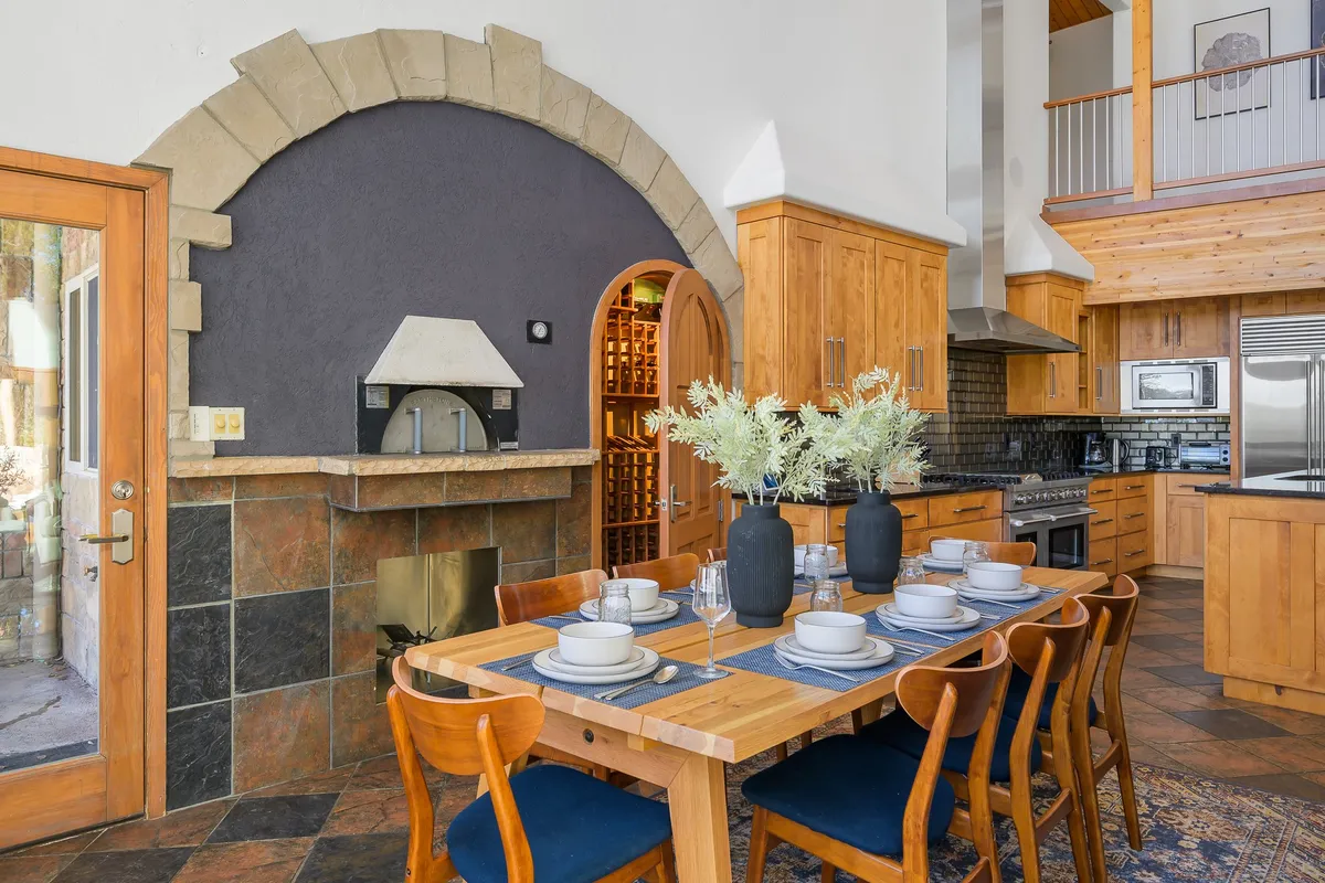 A warm, open dining area featuring a generous dining table, fireplace, visible kitchen space, and a wine storage nook. The scene invites large groups to share meals, laughter, and special occasions.