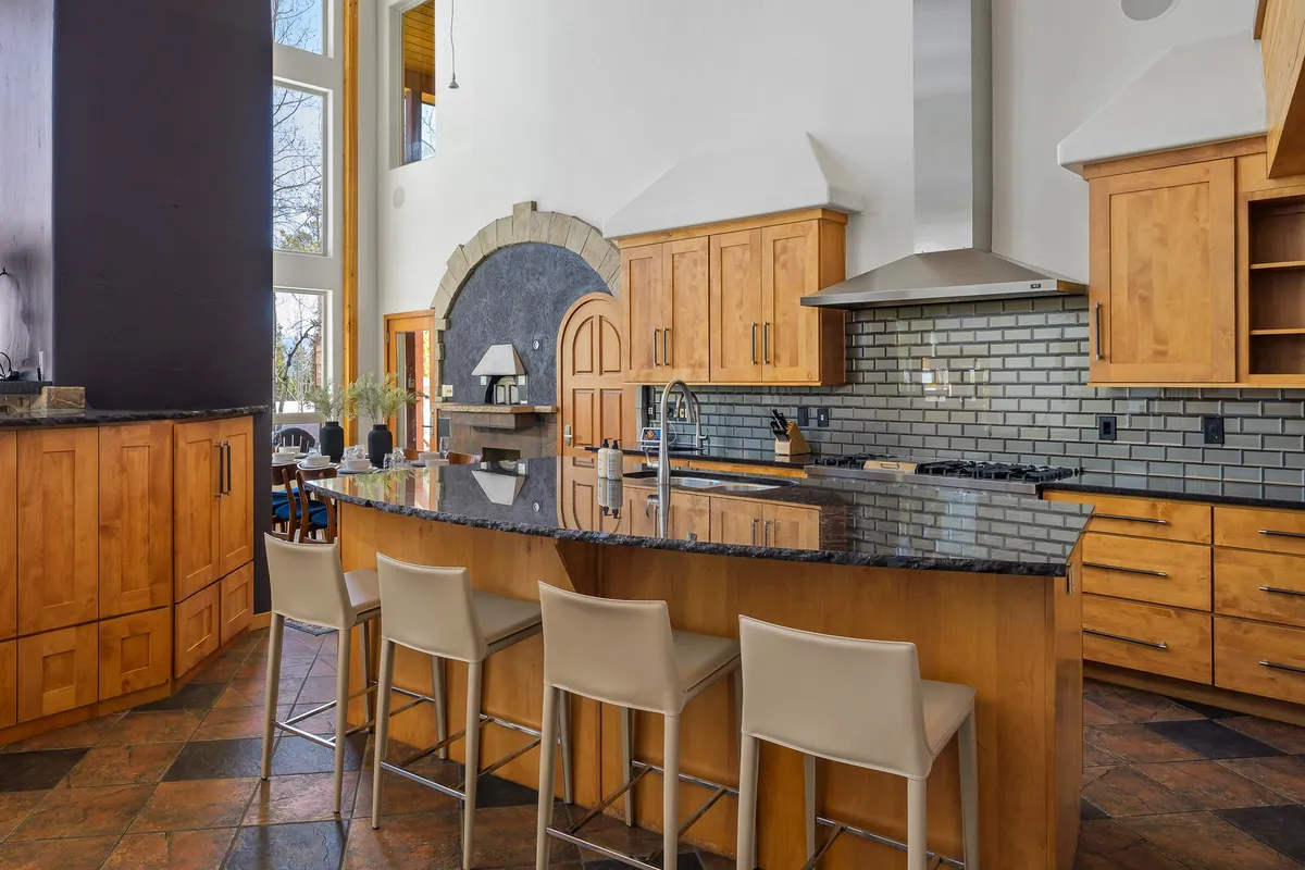 The kitchen’s large central island is surrounded by wooden cabinetry and gleaming stainless steel appliances. Expansive windows flood the space with light, creating an inviting, functional hub for cooking and conversation.