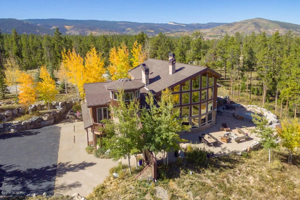 A welcoming exterior view of the home showcasing large windows, a stone facade, outdoor seating area, and lush natural surroundings. The house appears spacious and inviting, perfect for gatherings, with ample space on the patio for group activities or stargazing. The connection to the outdoors and the tranquility of the scene evoke a sense of communal enjoyment and relaxation.